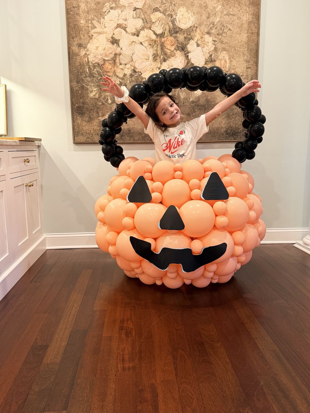 Smiling child standing inside a giant balloon pumpkin basket with arms in the air