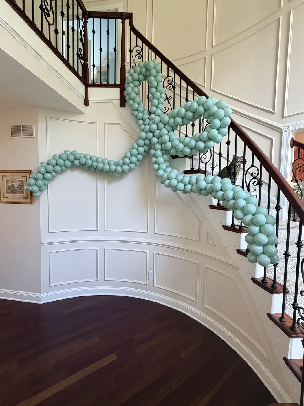 Oversized sage-green balloon bow draped along a curved staircase railing