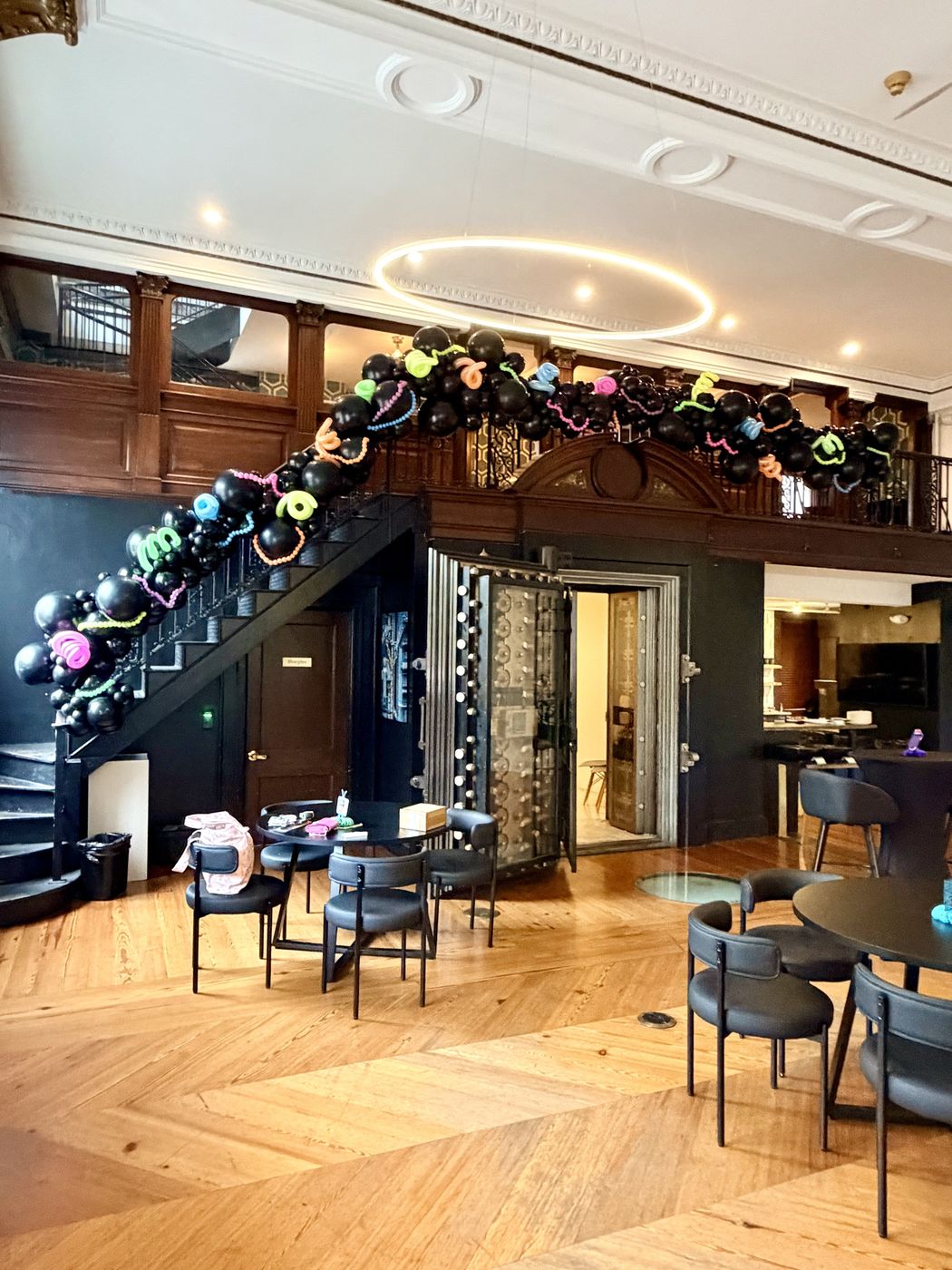 Black balloon garland with neon accents running up a venue staircase and across a balcony