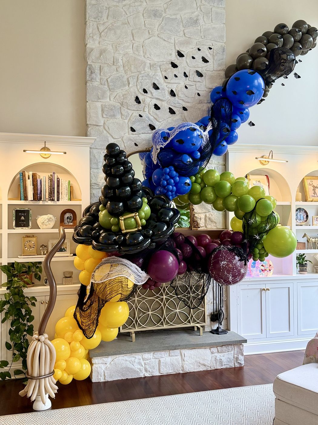 Large witch-themed balloon installation with a hat, broom and bats sweeping above a fireplace